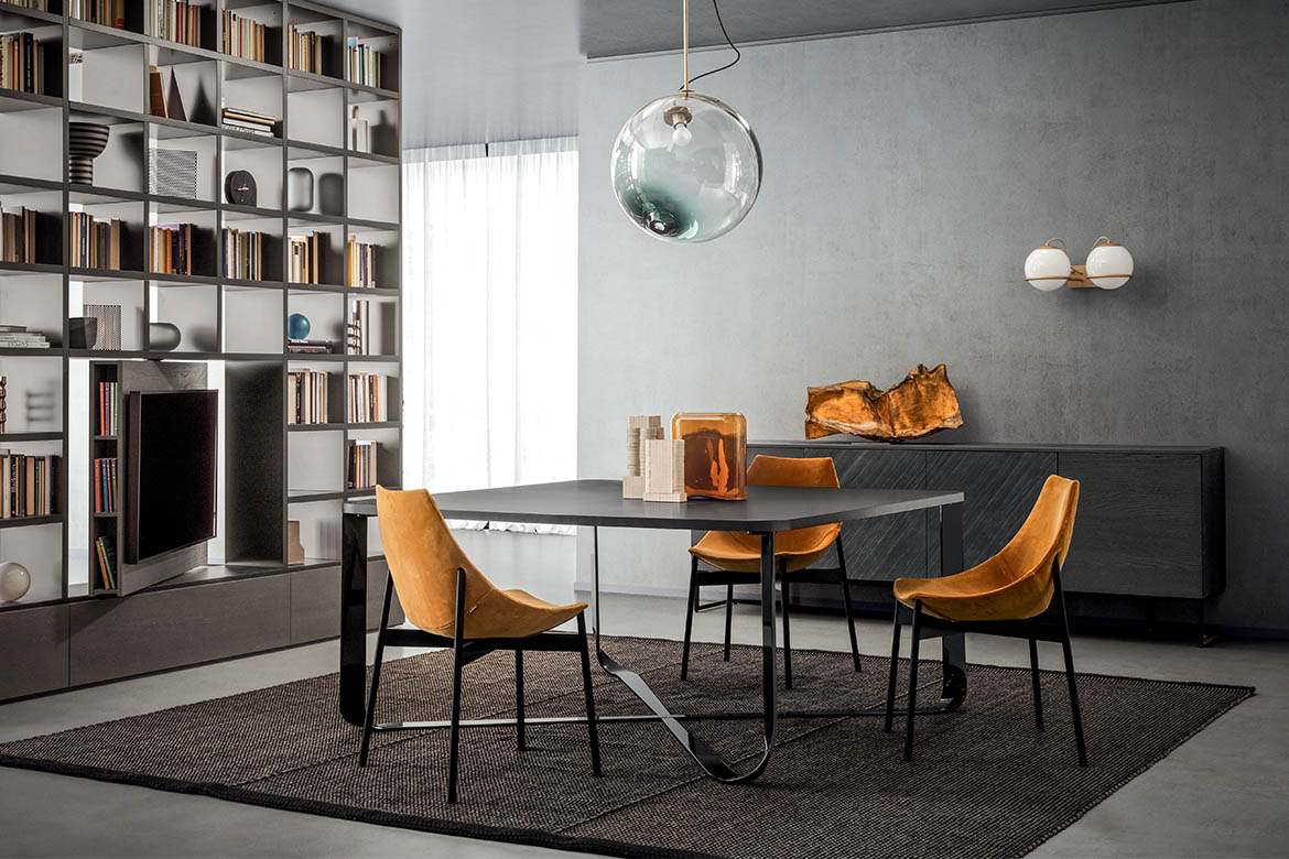 tavolo confluence quadrato con base in metallo curvato e piano in legno rovere grigio sedie imbottite in tessuto velluto giallo con bambe in tubolare laccate grigio lavagna libreria bifacciale con porta tv girevole